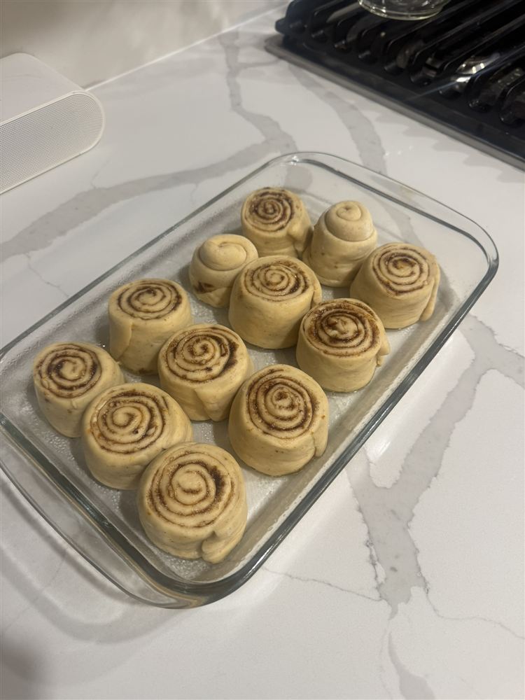 A dish of cinnamon rolls proofing on the kitchen counter