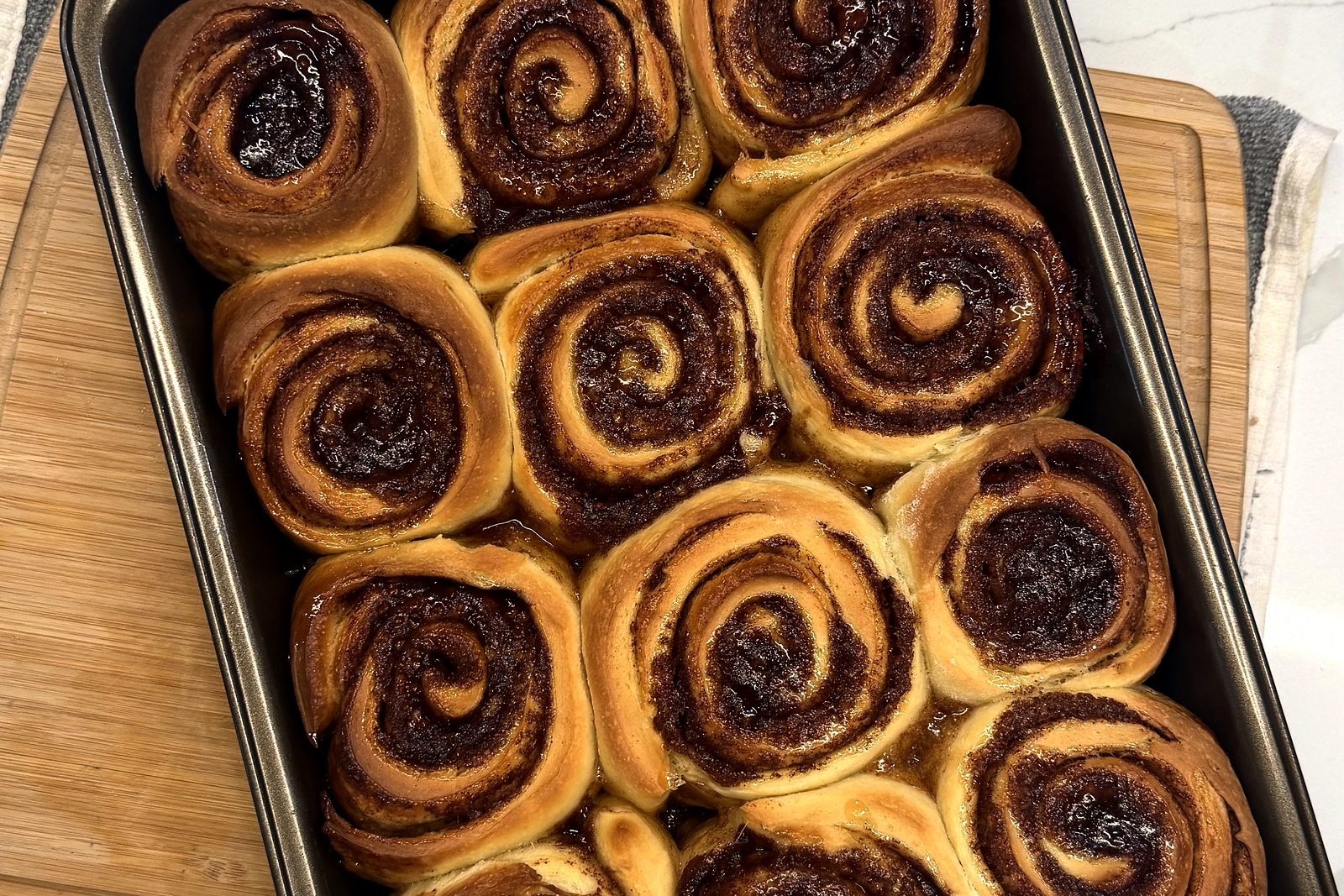 A dozen cinnamon rolls in the pan, fresh out of the oven, on the kitchen counter